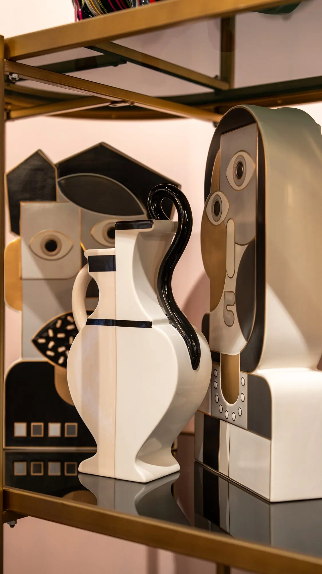 Vasi e volti in ceramica bianca e nera di ispirazione cubista su una mensola dorata.